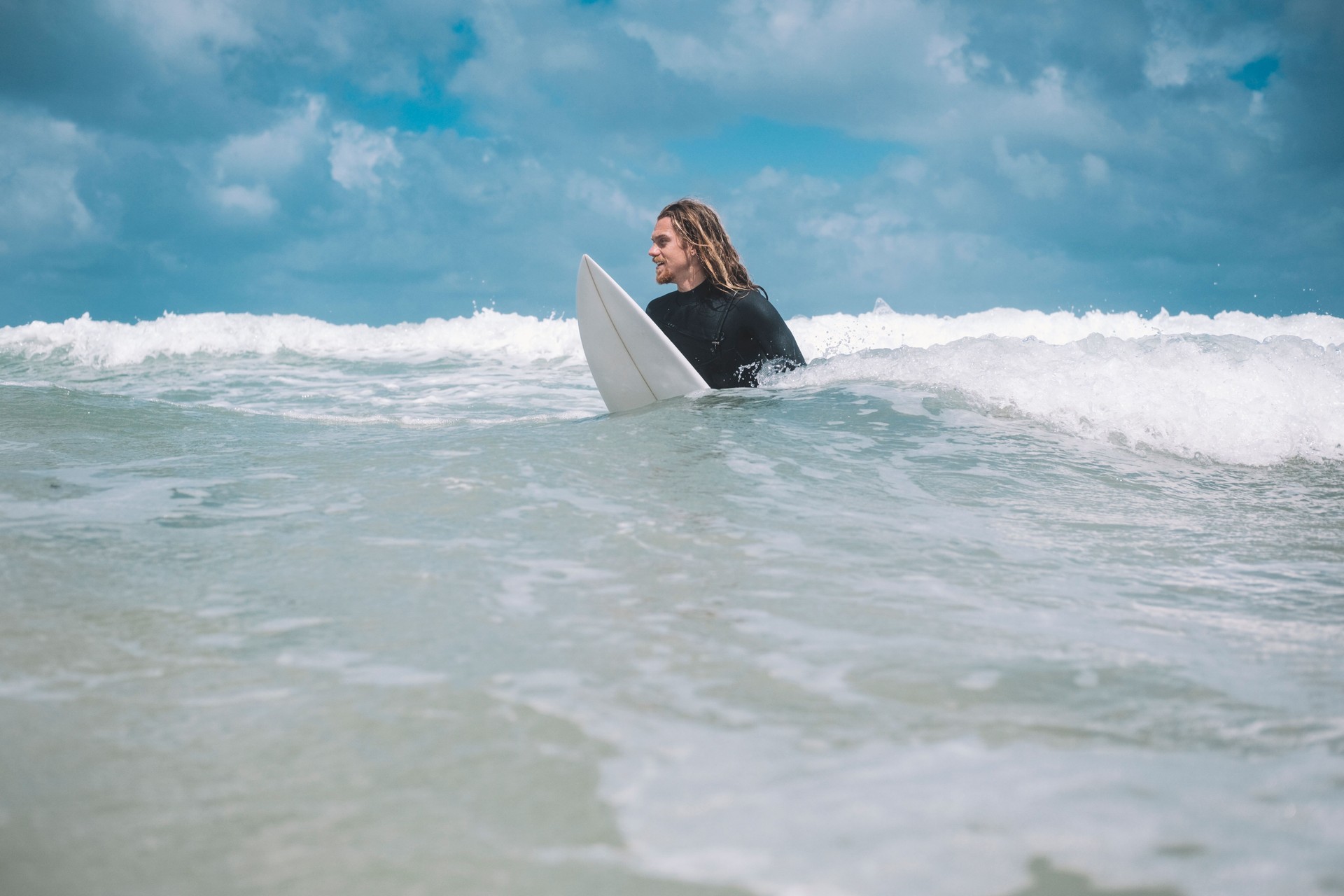 Male Surfer sitting on his surfboard in the sea, Newquay, Cornwall